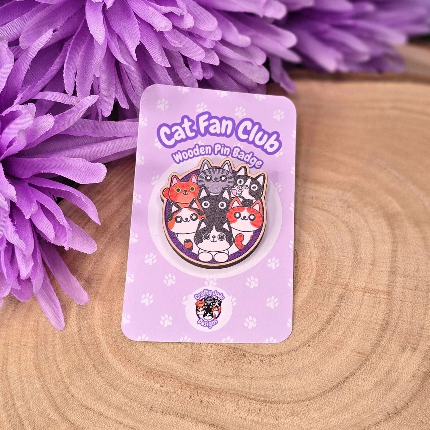 Cat-themed wooden pin badge on a purple card with purple flowers in the background