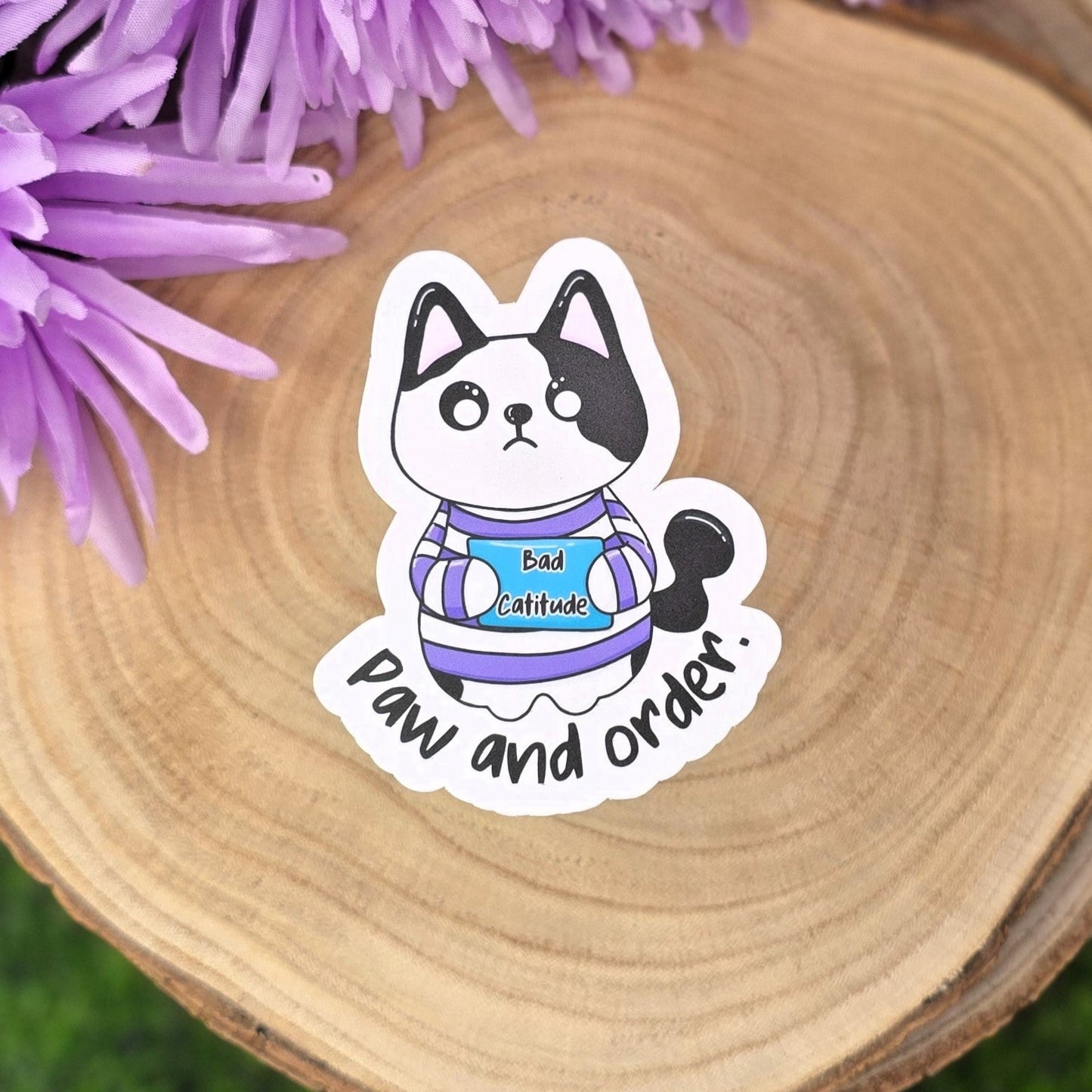 Sticker of a cat with text on a wooden surface with purple flowers