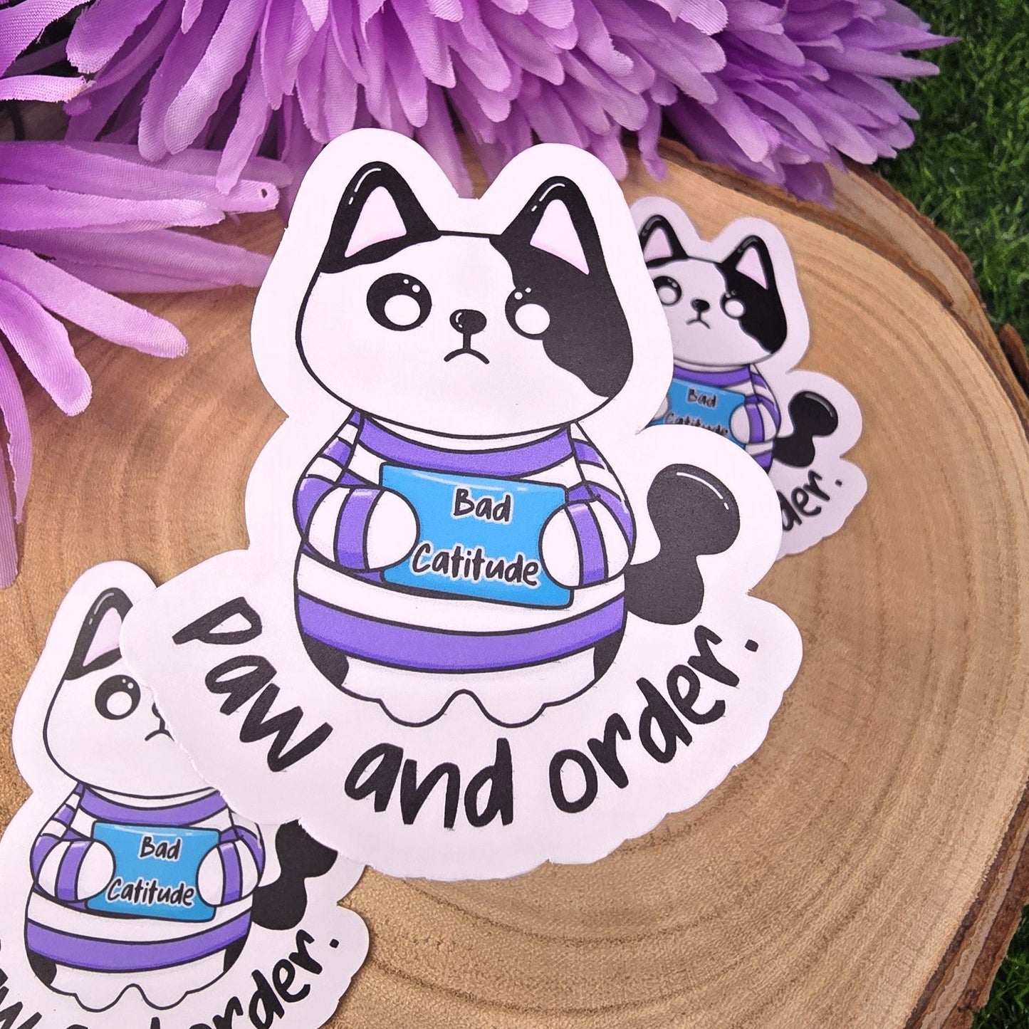 Sticker of a cat with text on a wooden surface with purple flowers in the background
