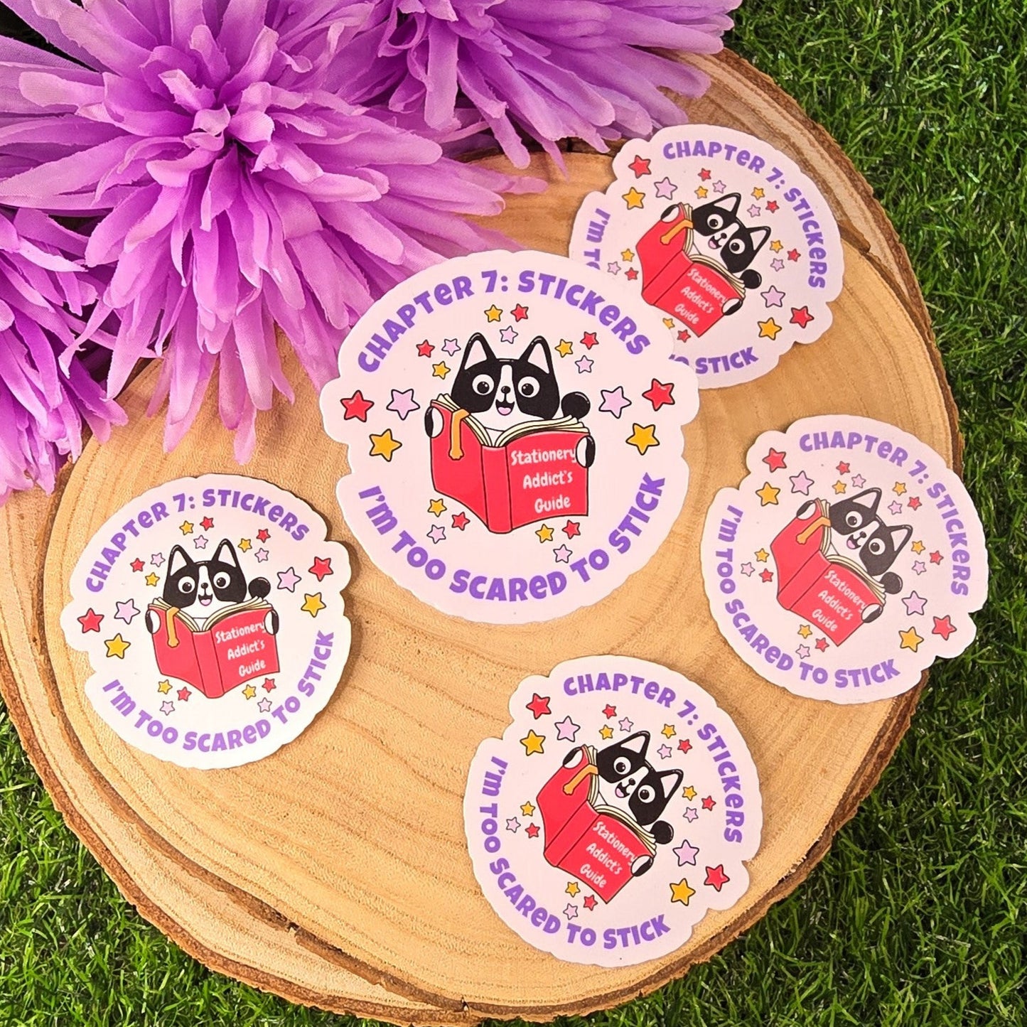 Stickers with a cat reading a book design on a wooden coaster with purple flowers in the background.