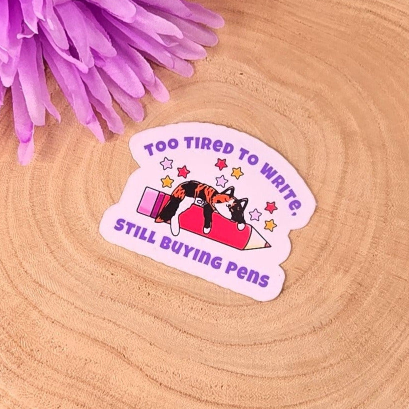 Sticker with a sleeping cat and text on a wooden disc with purple flowers