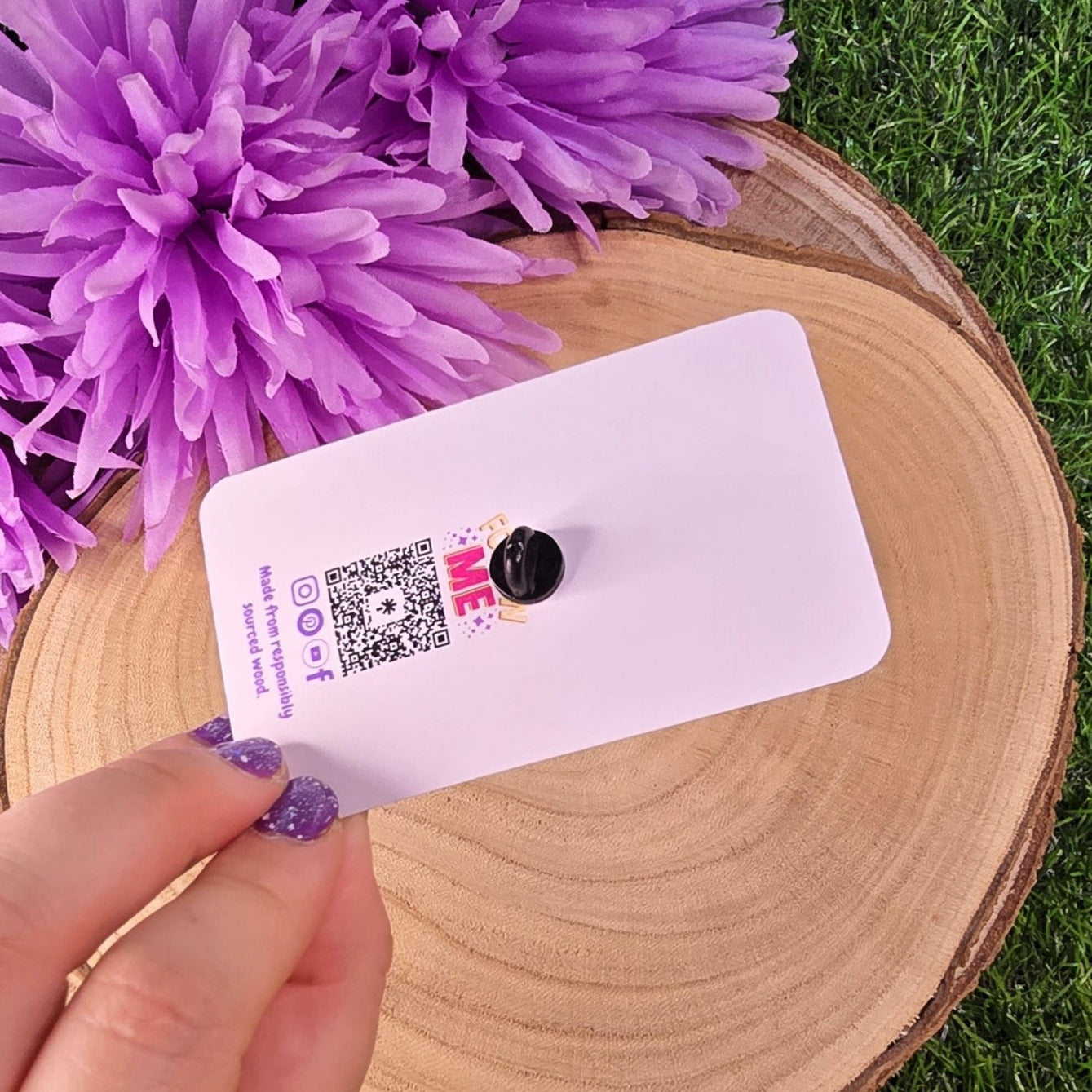 pin on a card with a QR code held by a hand, purple flowers in the background