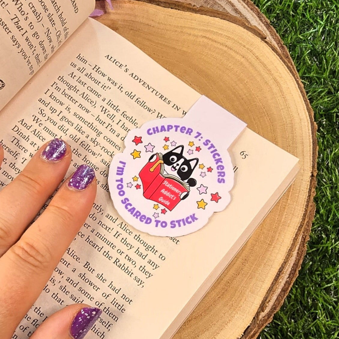 Hand holding a book with a bookmark 'I'm Too Scared to Stick' on a grassy background
