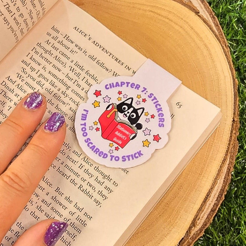 Hand holding a magnetic bookmark an open book on grass