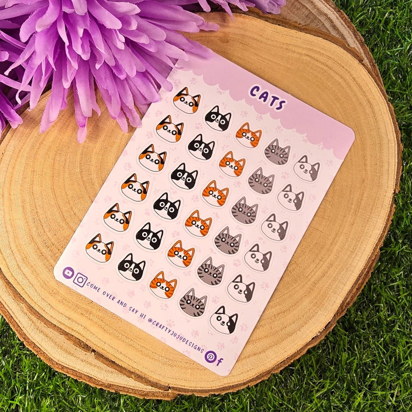 Sheet of cat-themed stickers on a wooden surface with purple flowers in the background