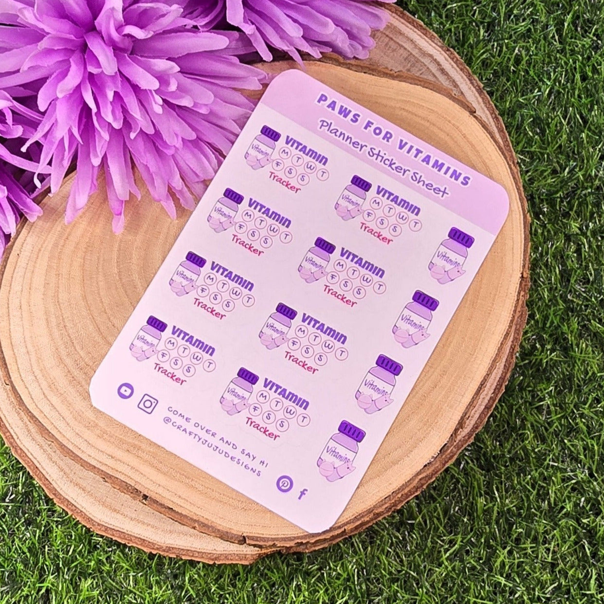 planner sticker sheet with product details on a wooden coaster with purple flowers on grass