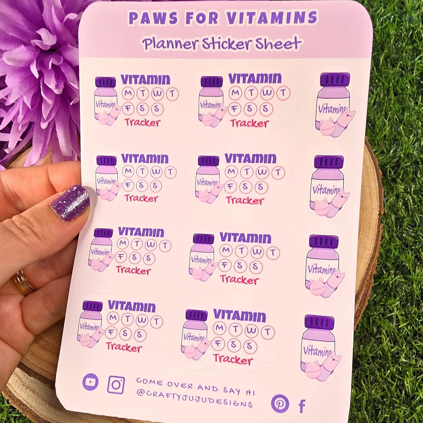 Sheet of planner stickers labeled 'Paws for Vitamins' held over grass with a purple flower.