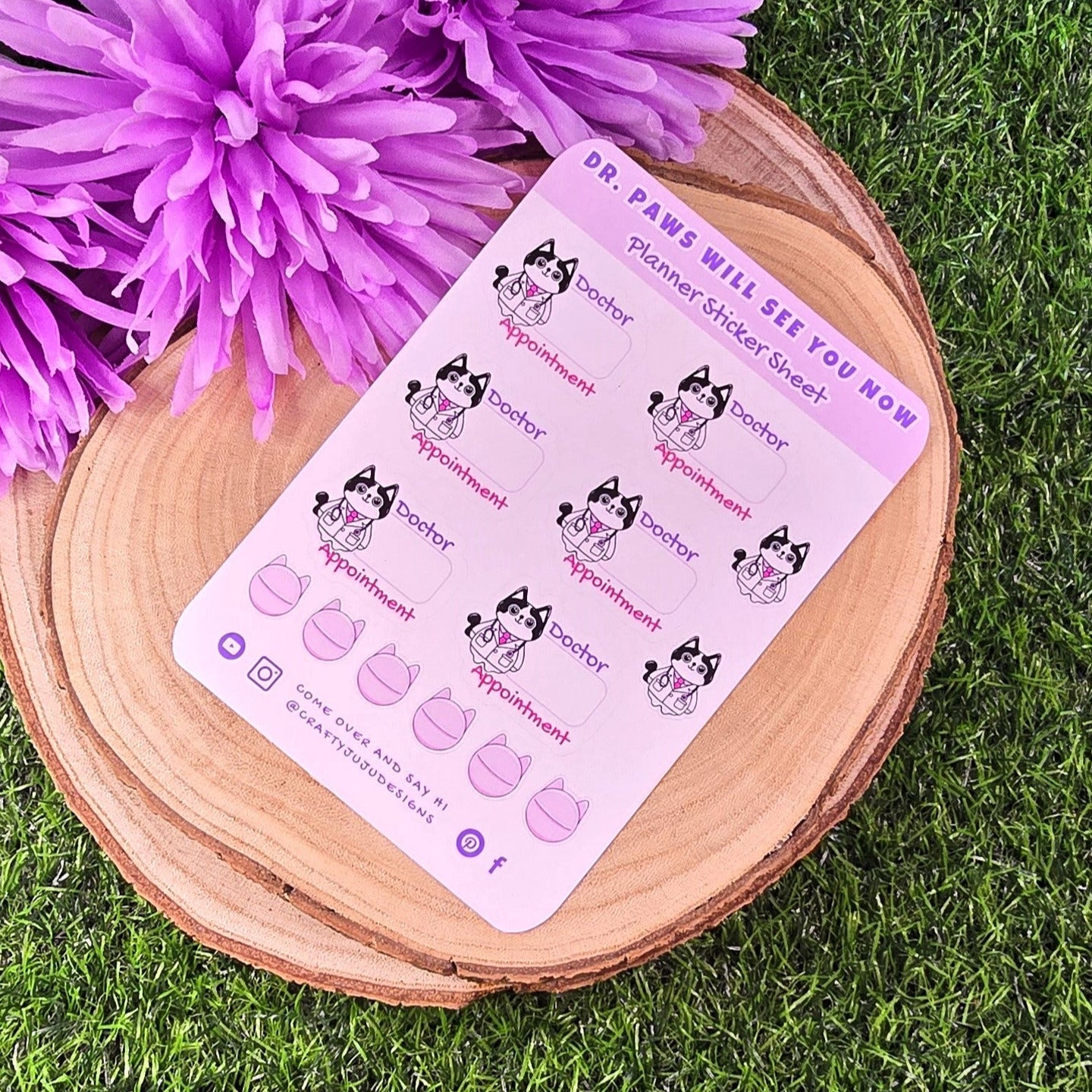 planner sticker sheert with cat designs on a wooden stand with purple flowers on grass