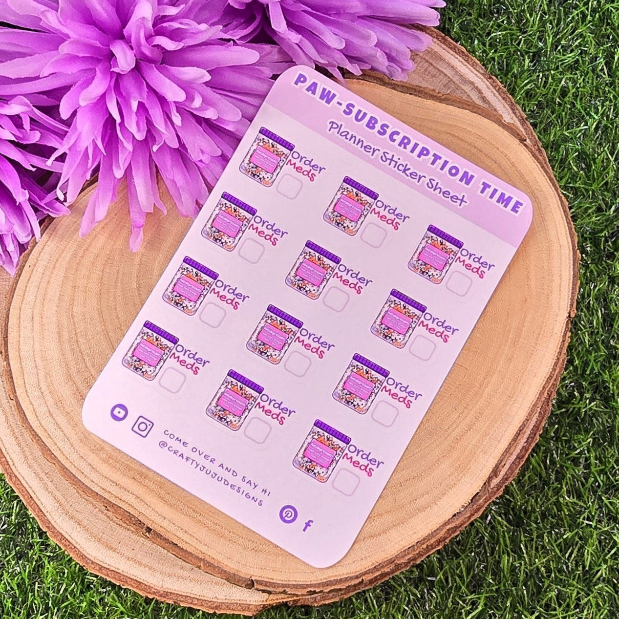 Sheet of planner stickers with paw print design on a wooden board with purple flowers on grass.
