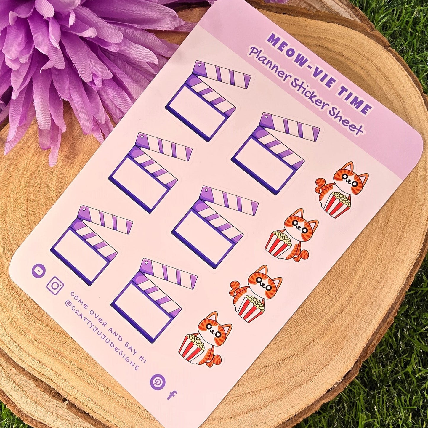 Sticker sheet with cat designs on a wooden surface with purple flowers in the background