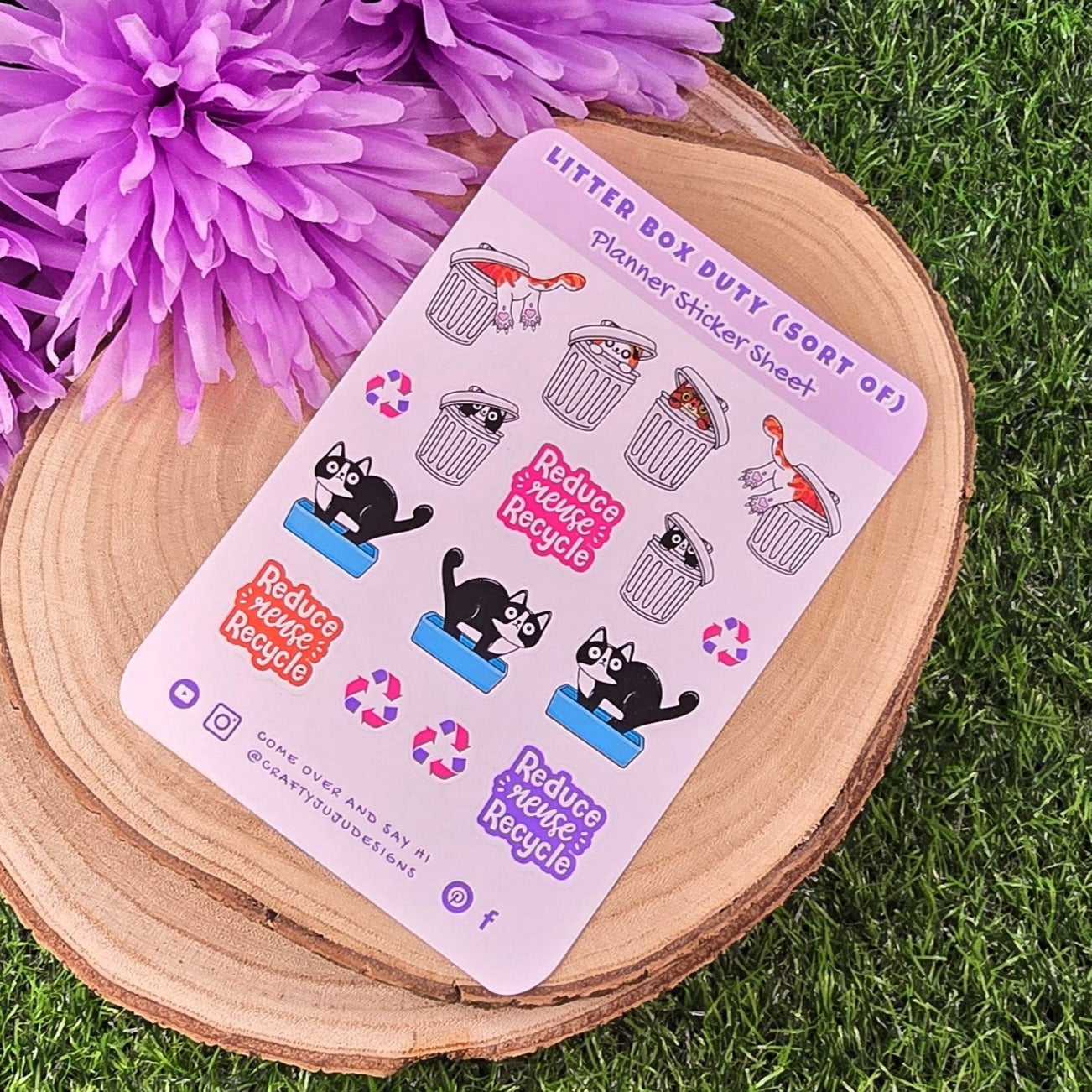 Sticker sheet with cat-themed designs on a wooden platform with purple flowers and grass in the background