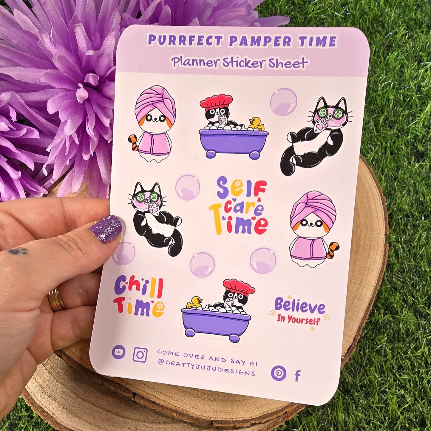 Sticker sheet with self-care-themed designs held by a hand on grass with purple flowers.