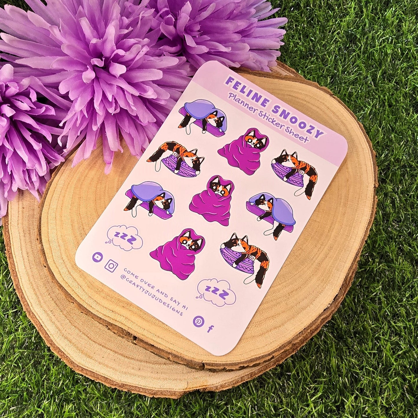 Sheet of stickers with cat illustrations on a wooden coaster with purple flowers in the background
