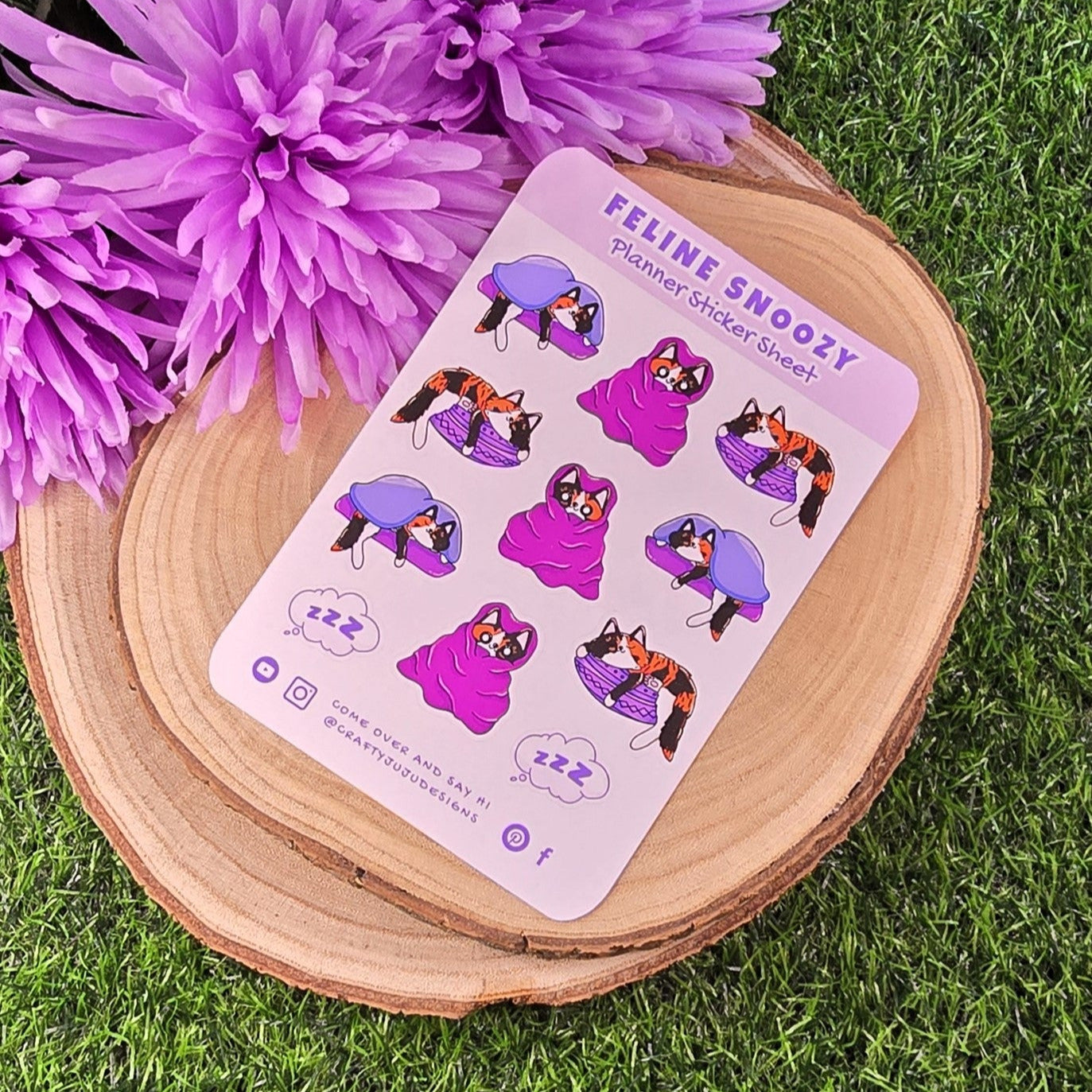 Sticker sheet with cat illustrations on a wooden block with purple flowers in the background