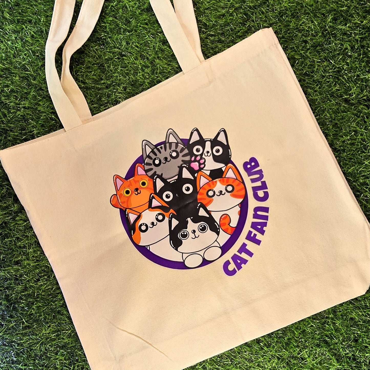 Beige tote bag with cat-themed design and 'Cat Fan Club' text on grass