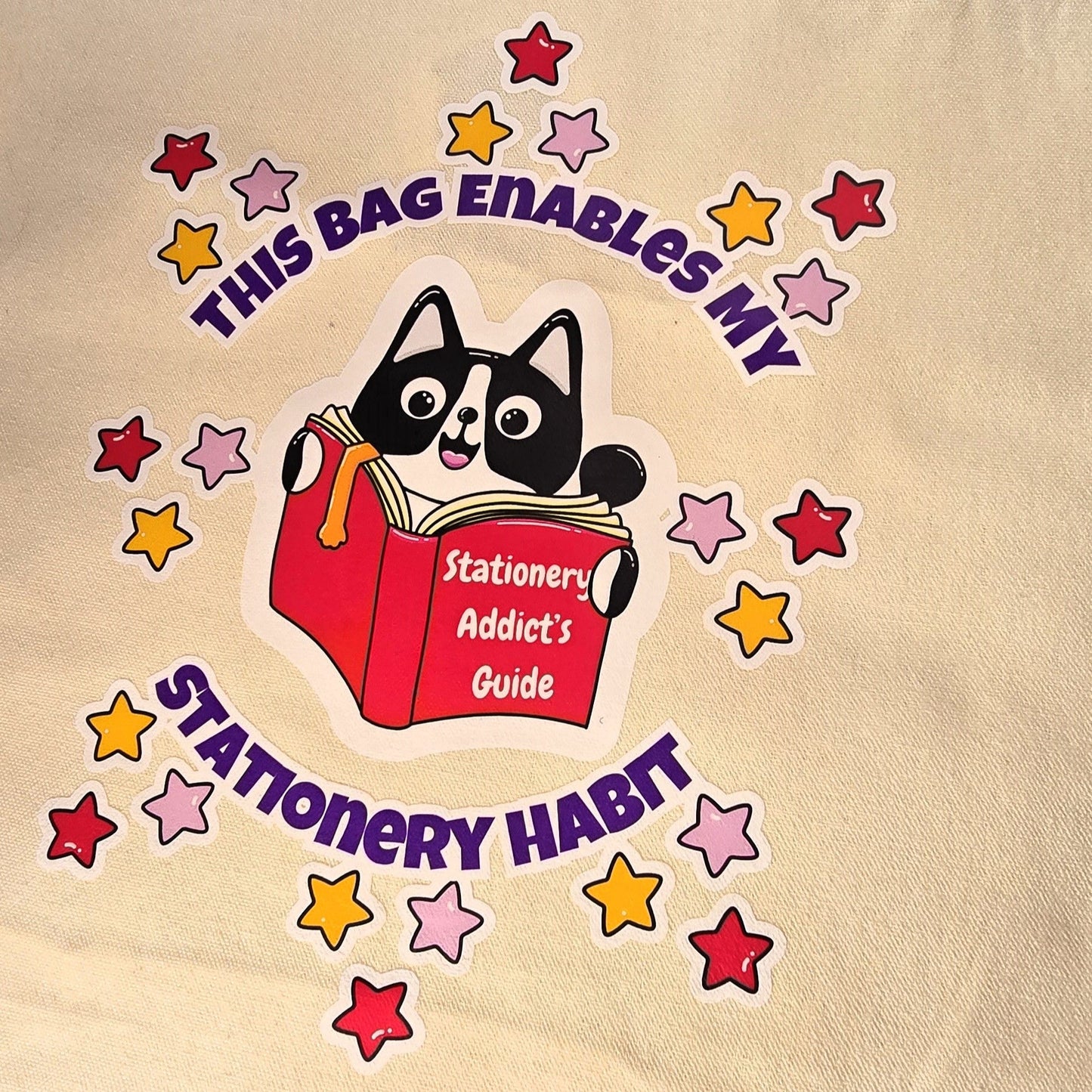 Beige tote bag with a cat graphic and text on grass