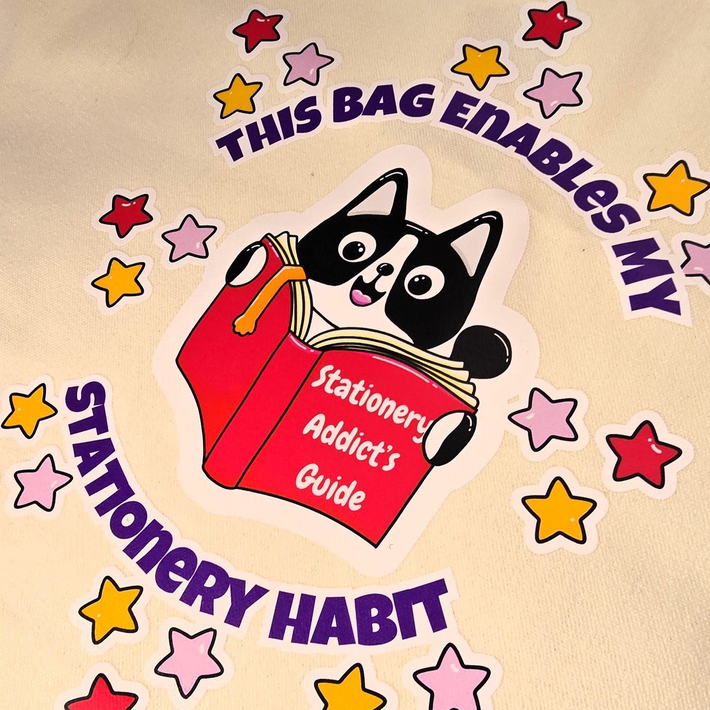Beige tote bag with cartoon cat holding a book and text on grass