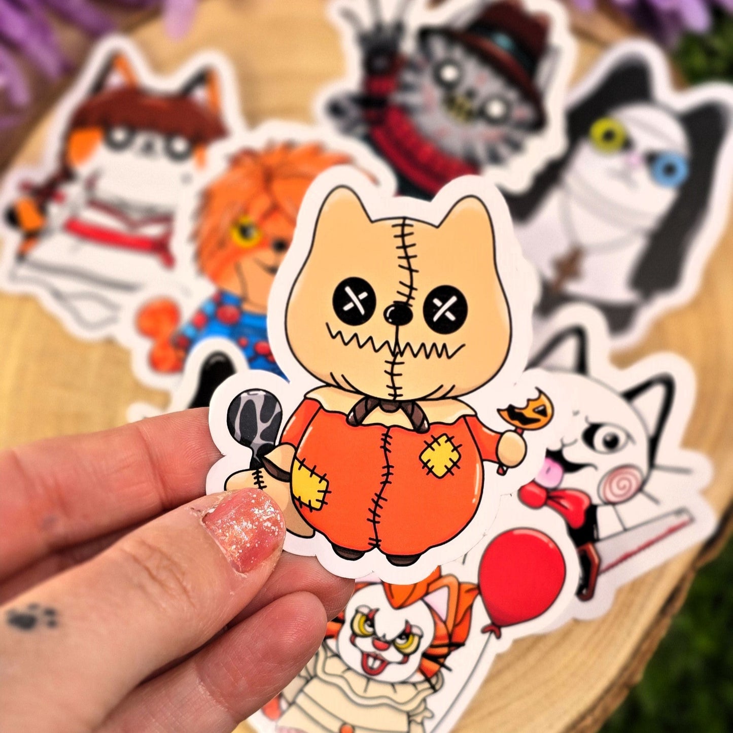 Hand holding a sticker of a cat in a pumpkin costume with other Halloween-themed stickers in the background.