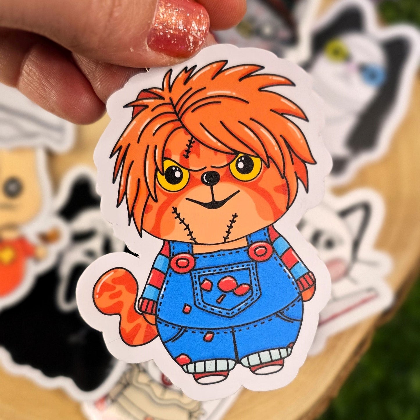 Cartoon character sticker with orange hair and blue overalls held by a hand on a grassy background.
