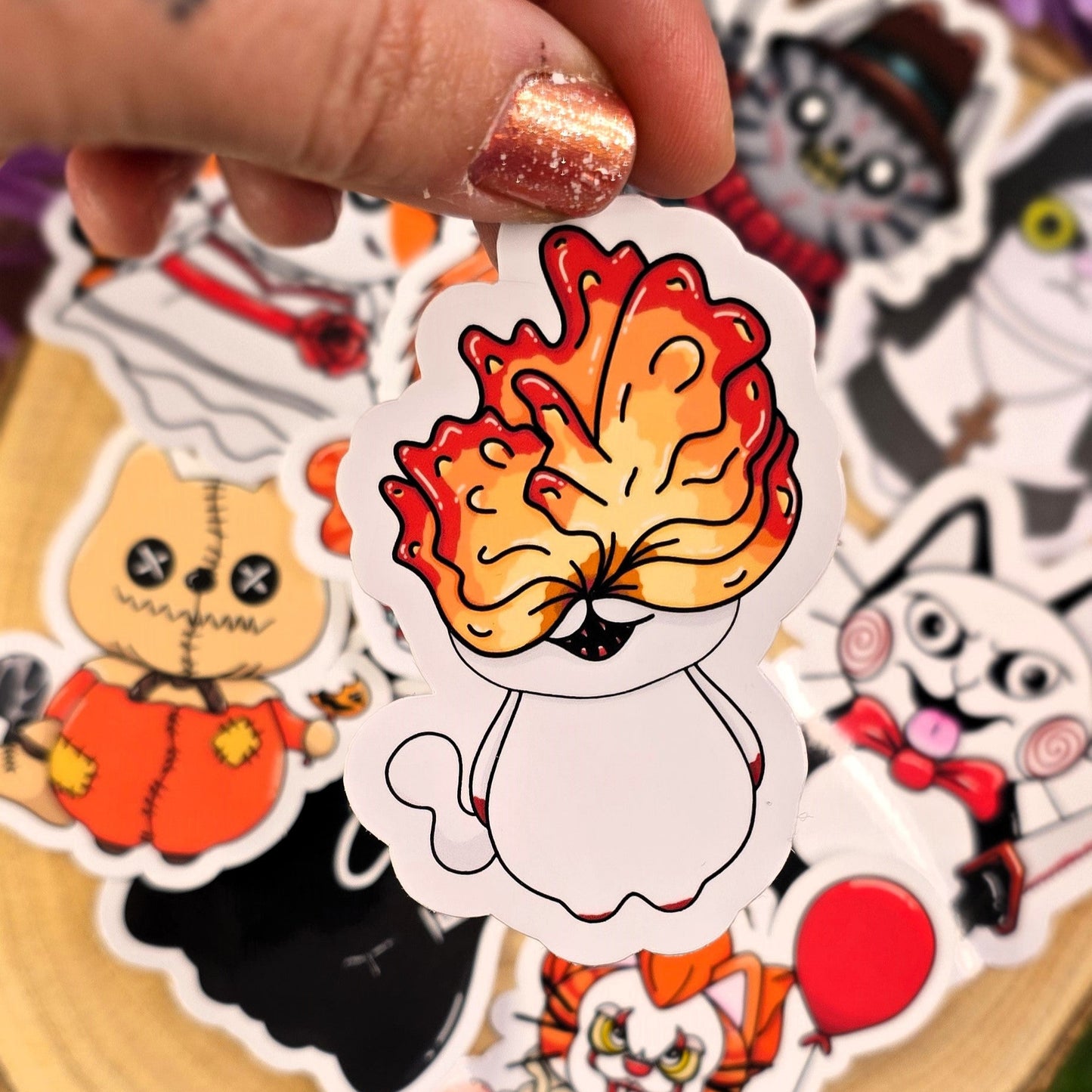 Hand holding a sticker with a cartoon character with orange hair on a wooden surface with other stickers.