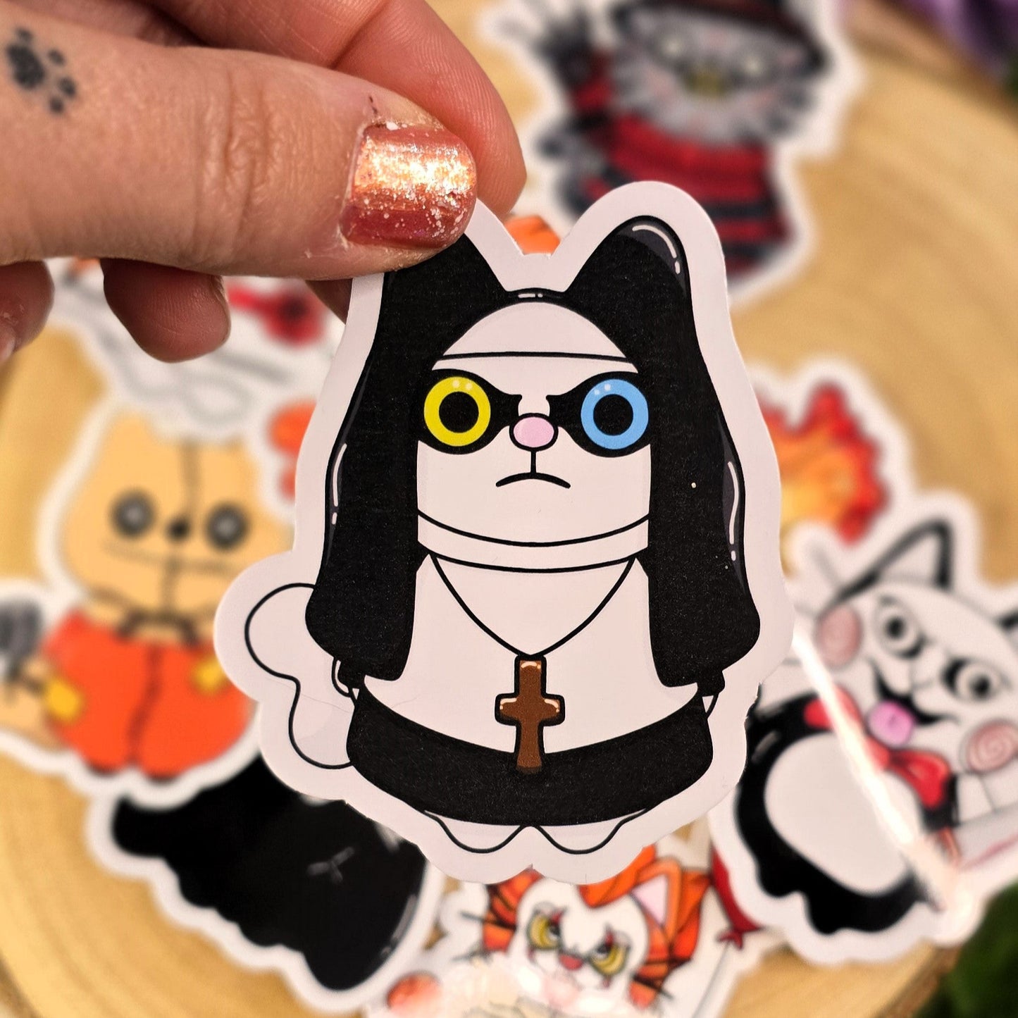 Sticker of a cartoon nun held by a hand on a wooden surface with other stickers in the background.