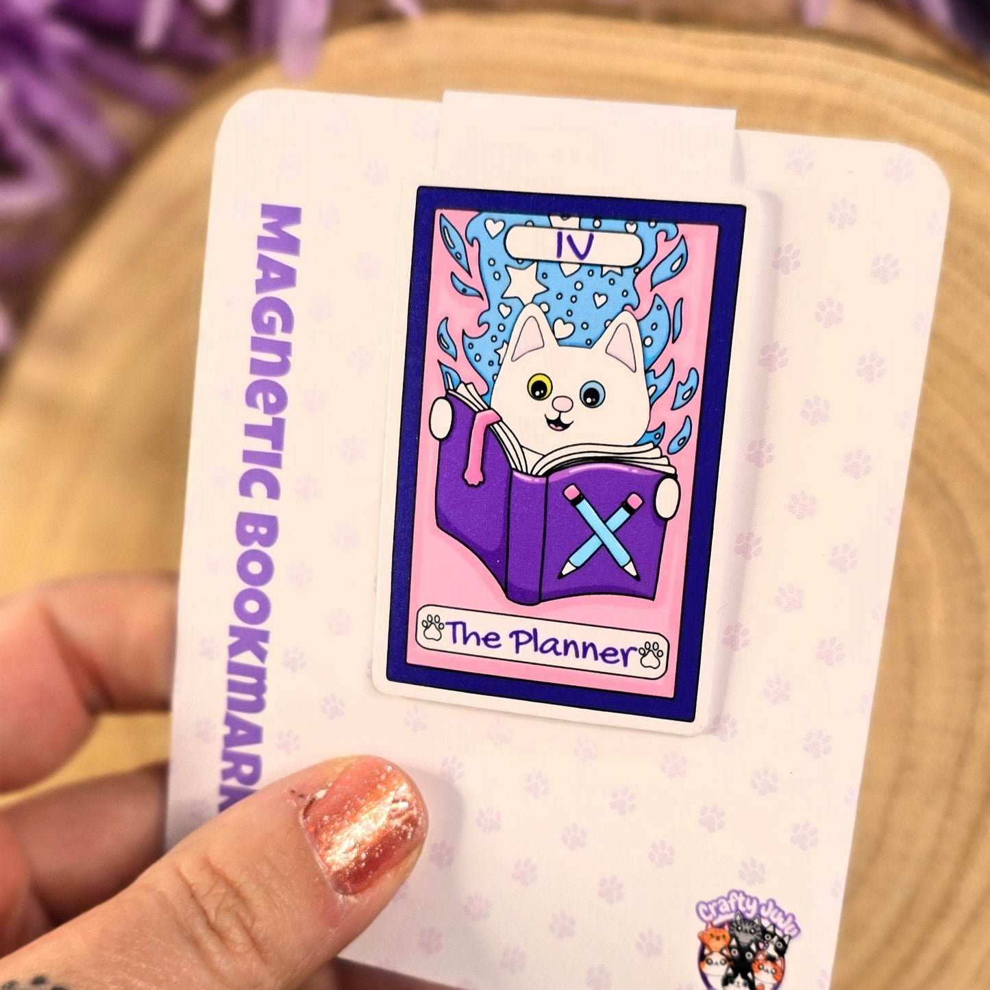 Magnetic bookmark with cartoon design held by a hand against a purple flower background