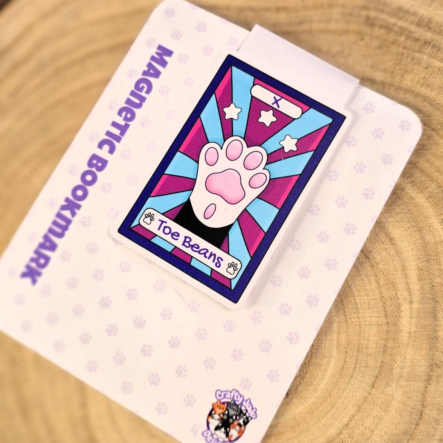 Magnetic bookmark with paw design on a wooden surface with purple flowers in the background