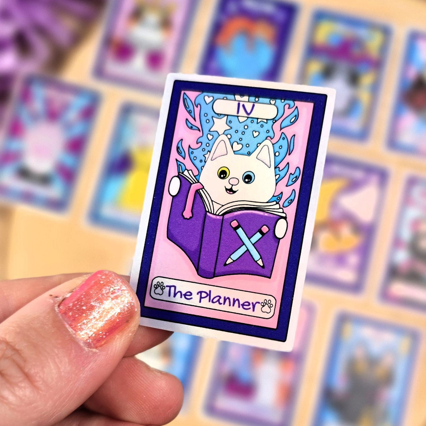 sticker with a cat illustration and 'The Planner' text held by a hand, with more cards in the background.