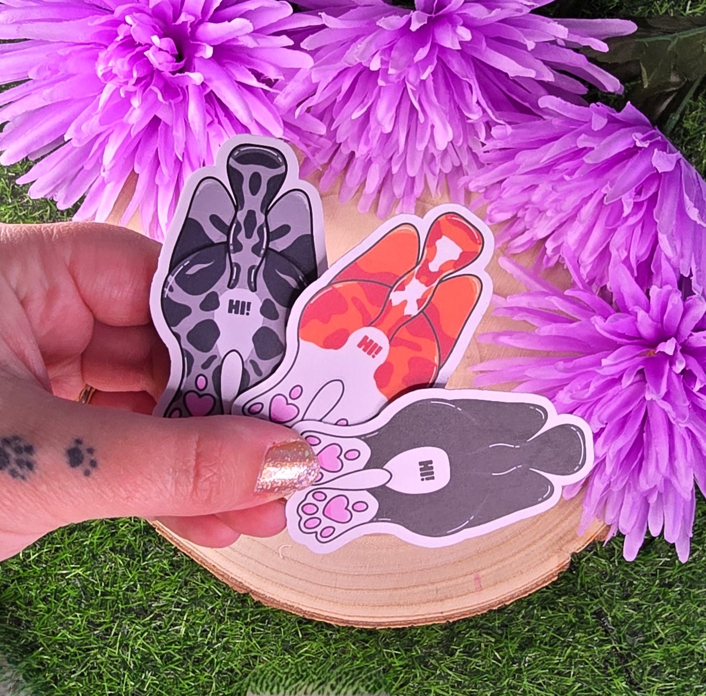 Hand holding three stickers with paw prints against a background of purple flowers.