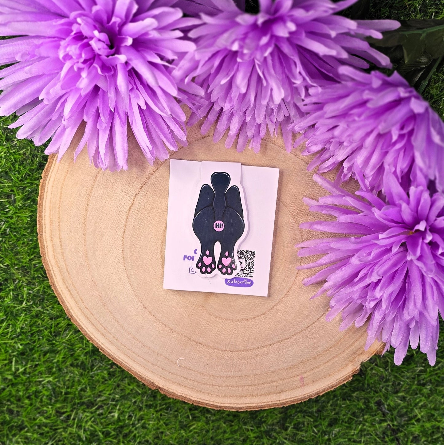 Card with a black cat illustration on a wooden platform surrounded by purple flowers.