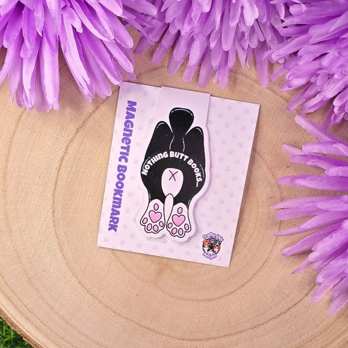 Magnetic bookmark with foot design on a card, surrounded by purple flowers on a wooden surface