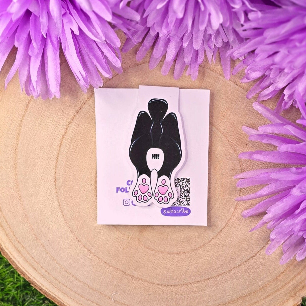 Card with a black and white illustration of a hand holding a heart, surrounded by purple flowers on a wooden surface.