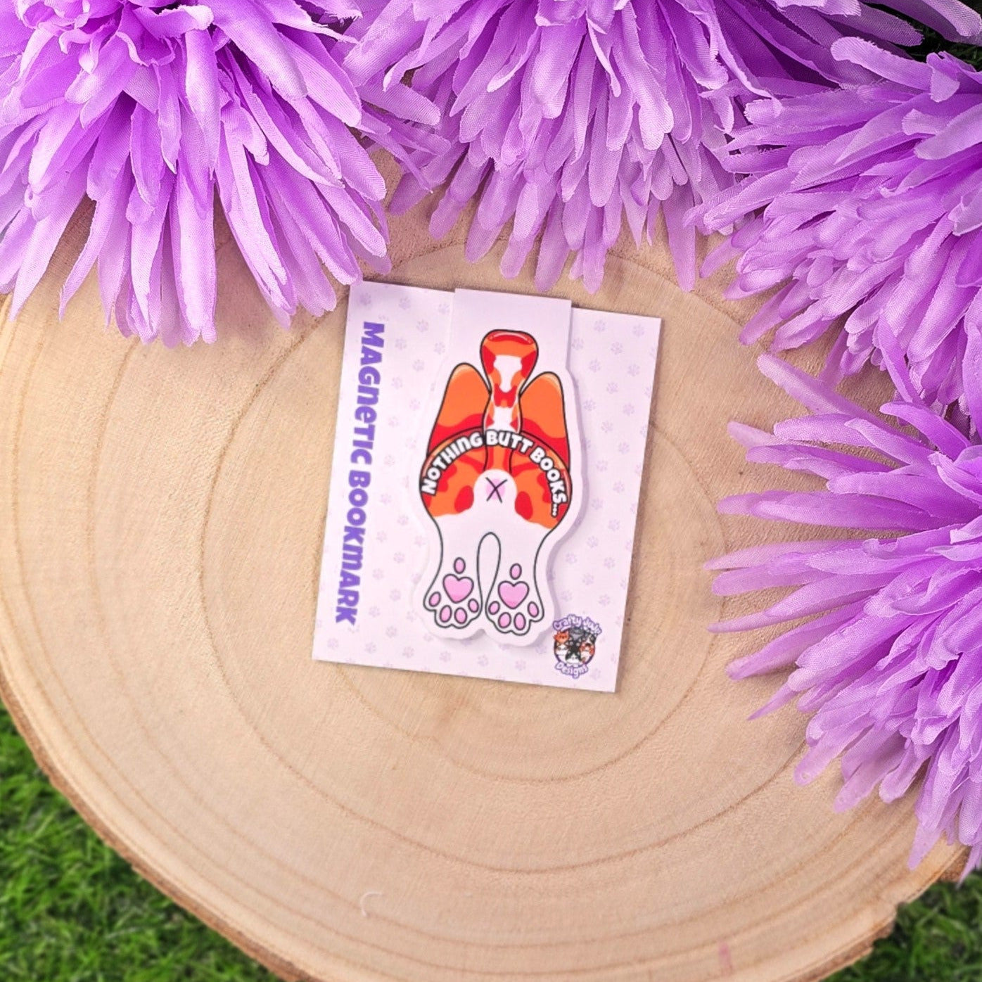 Magnetic bookmark with cartoon design on a wooden surface surrounded by purple flowers