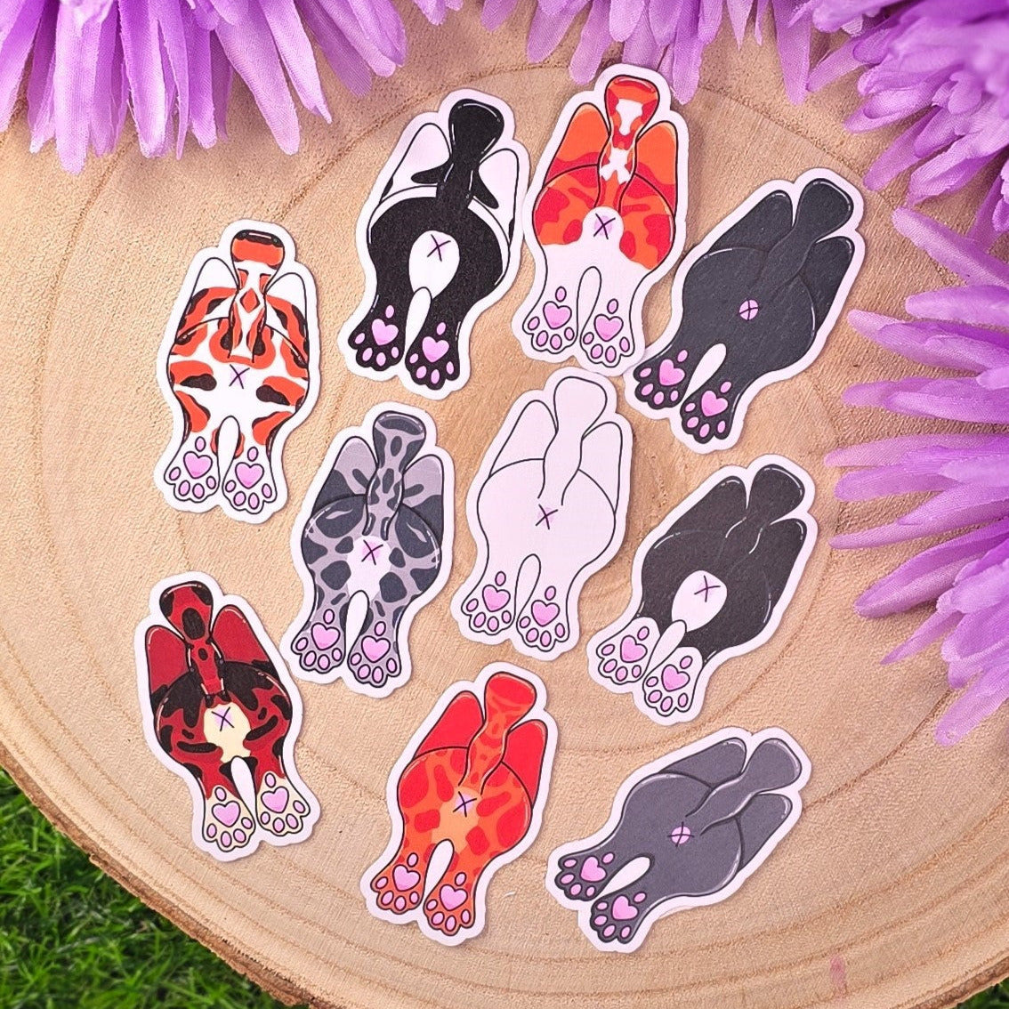 Set of cat butt stickers on a wooden surface with purple flowers.