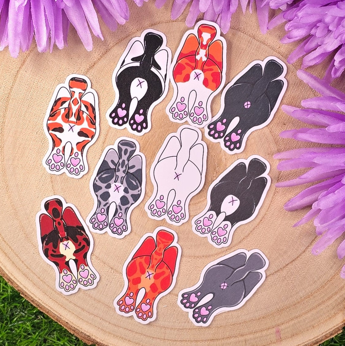 Set of colorful cat butt stickers on a wooden surface with purple flowers.