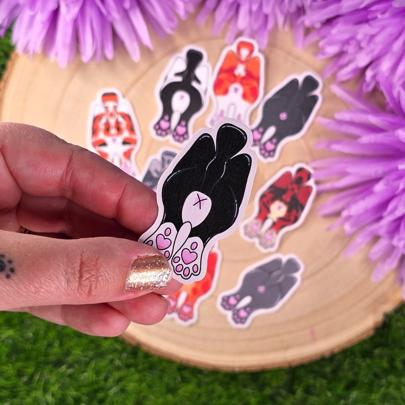 Sticker pack with cats showing off their butts illustrations on a wooden log with purple flowers in the background