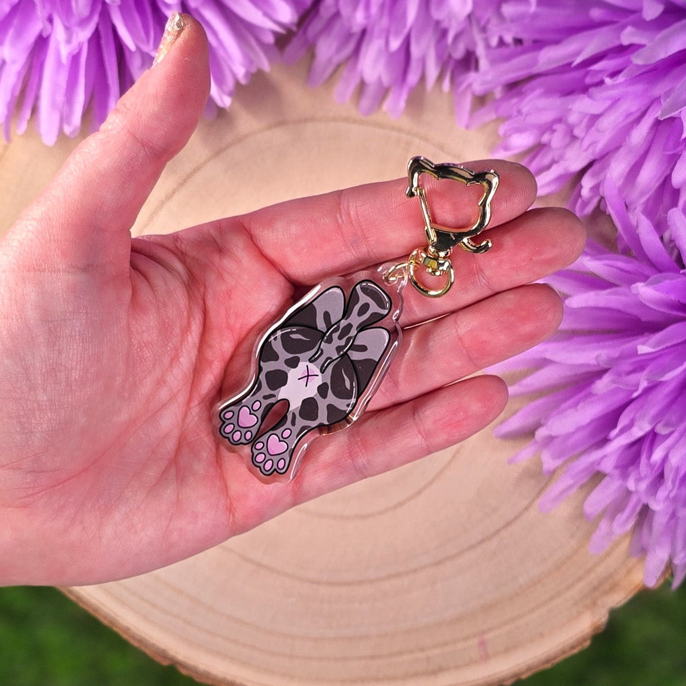 Hand holding a keychain with a cat butt design against a purple floral background