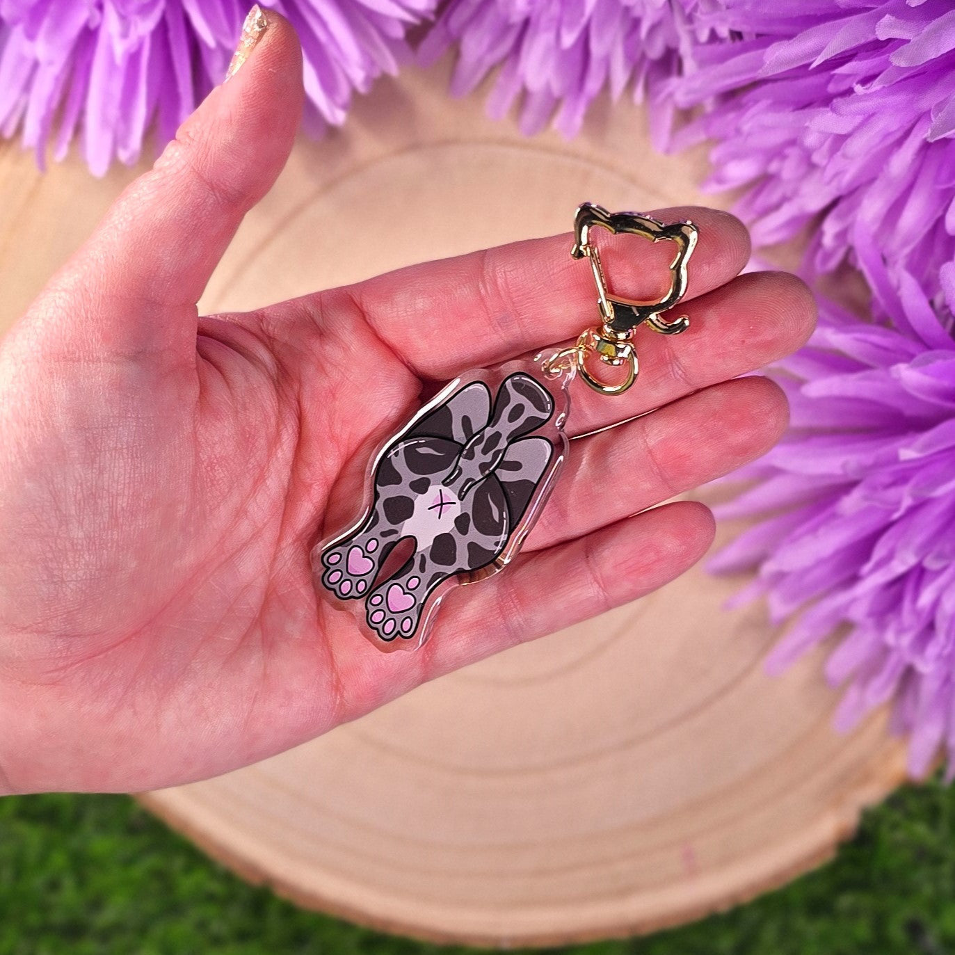 Hand holding a keychain with a cat design against a purple floral background