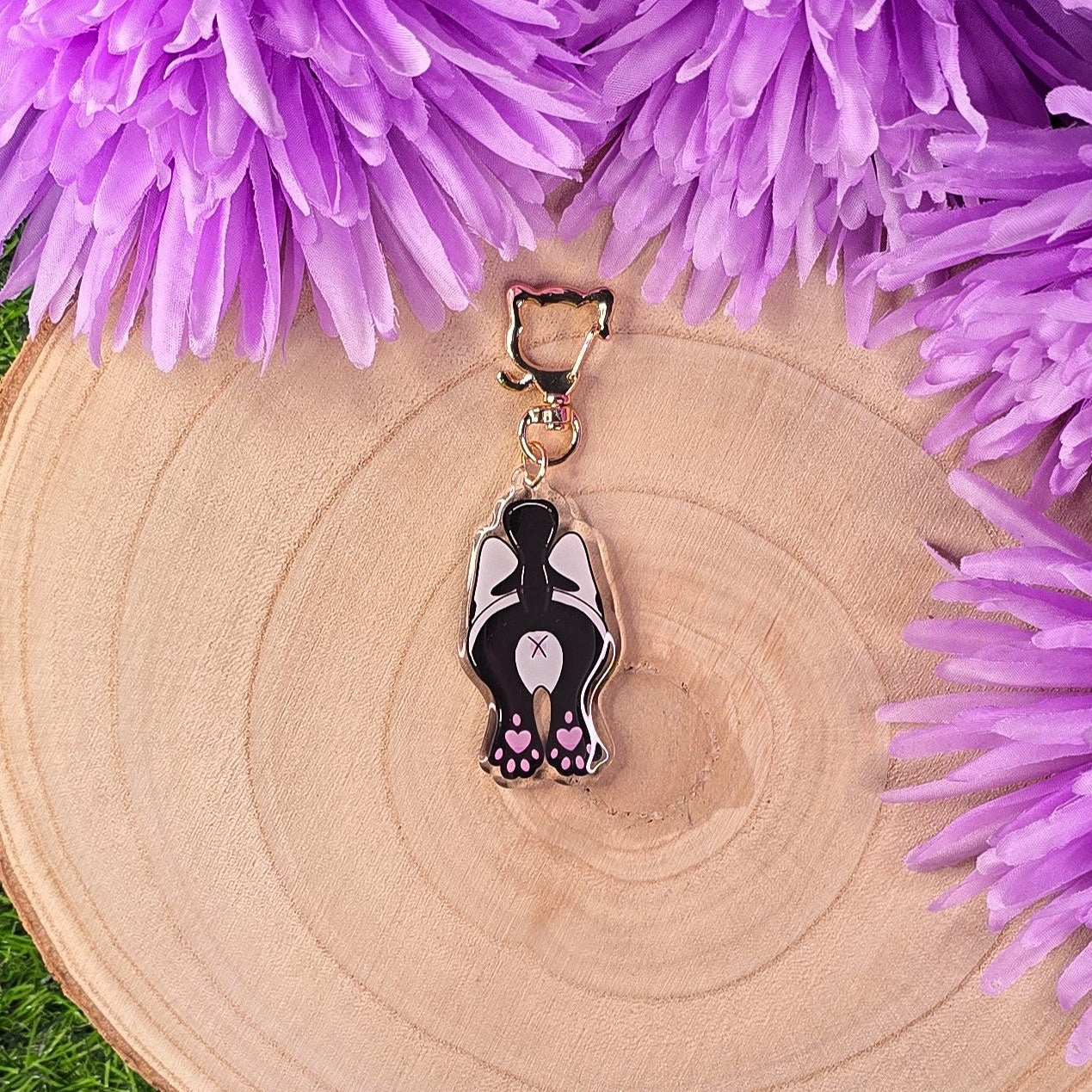 cat butt keyring on a wooden surface surrounded by purple flowers.