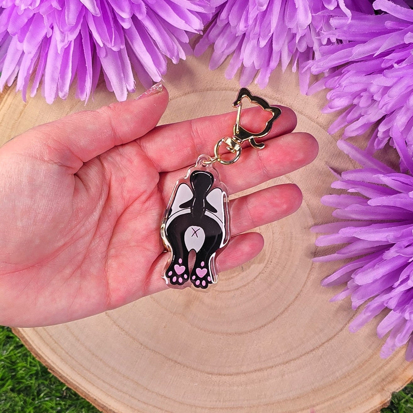 Hand holding a cat-shaped keychain with purple flowers in the background