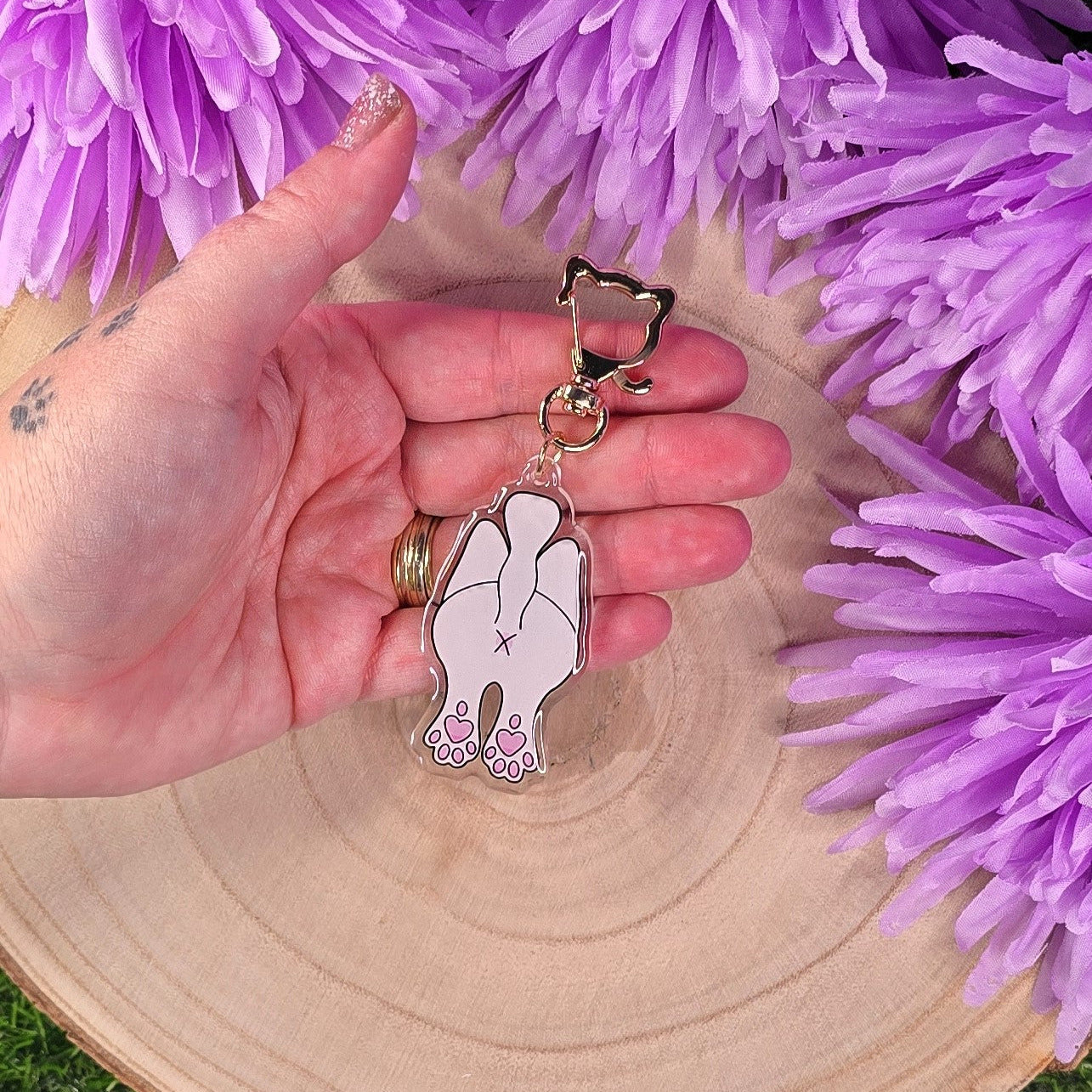 Hand holding a keychain with a cat design against a purple flower background