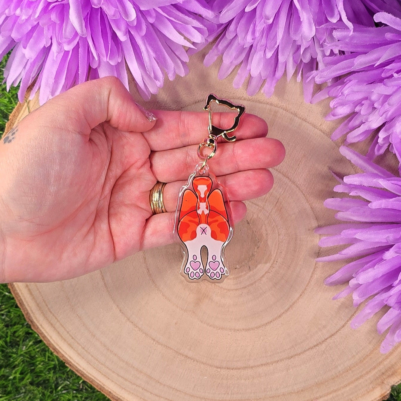 cat butt keyring on a wooden surface surrounded by purple flowers