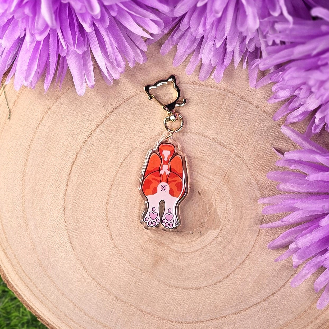 cat butt keyring on a wooden surface surrounded by purple flowers