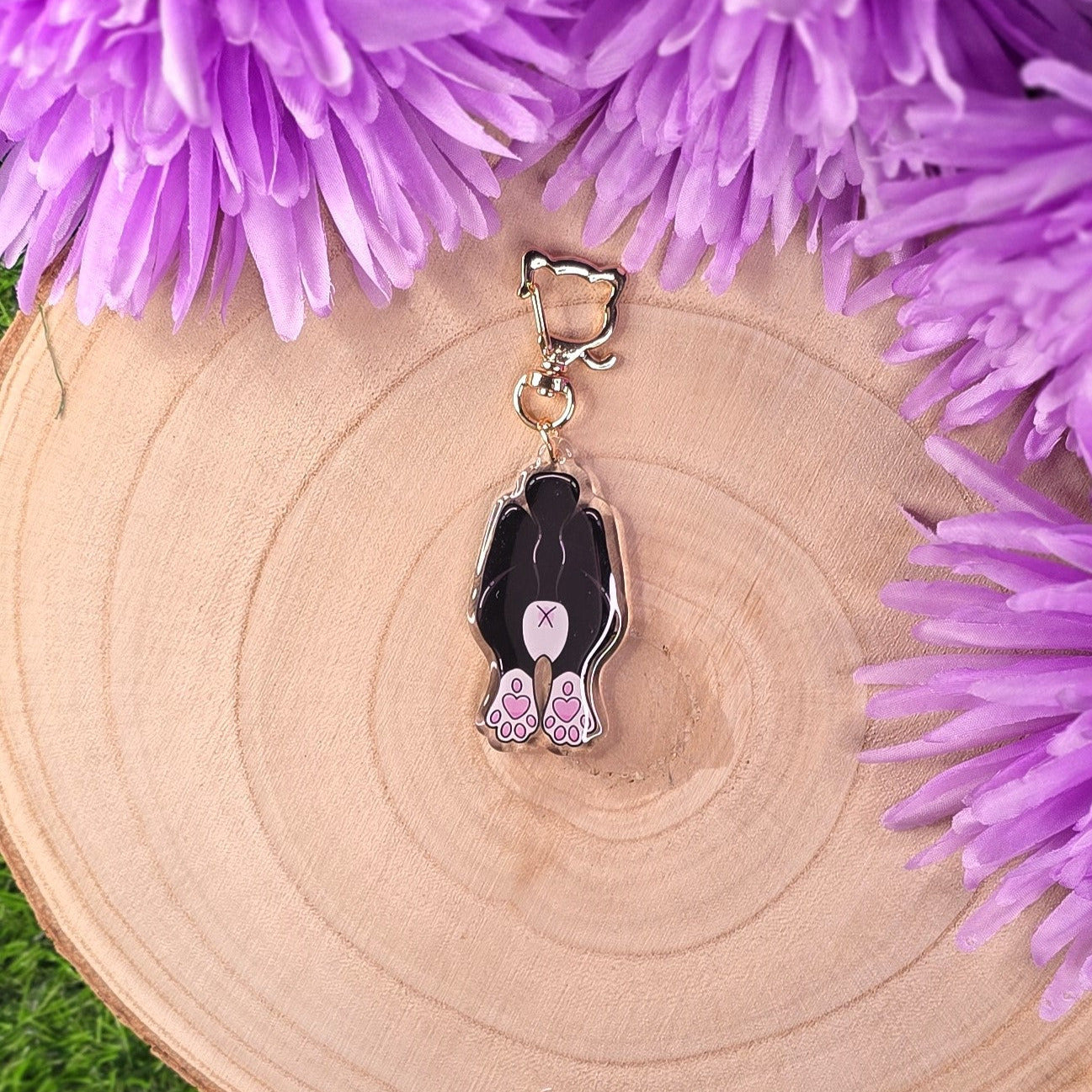 Keychain with a cat butt design on a wooden surface with purple flowers