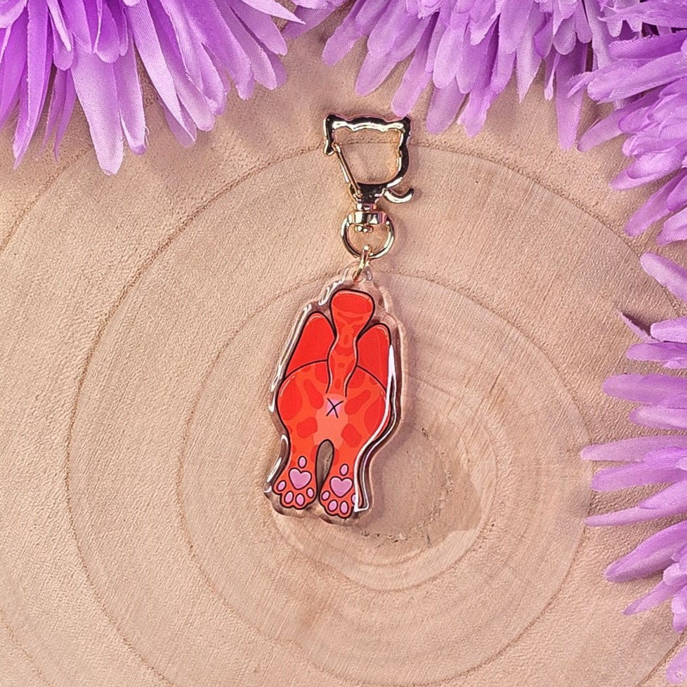 cat butt keyring on a wooden surface surrounded by purple flowers