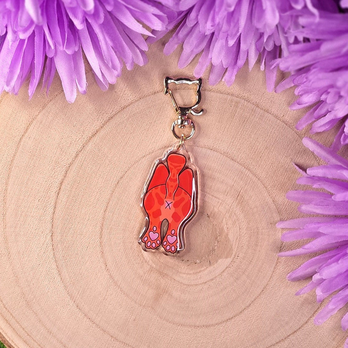cat butt keyring with a cat head clip on a wooden surface with purple flowers.