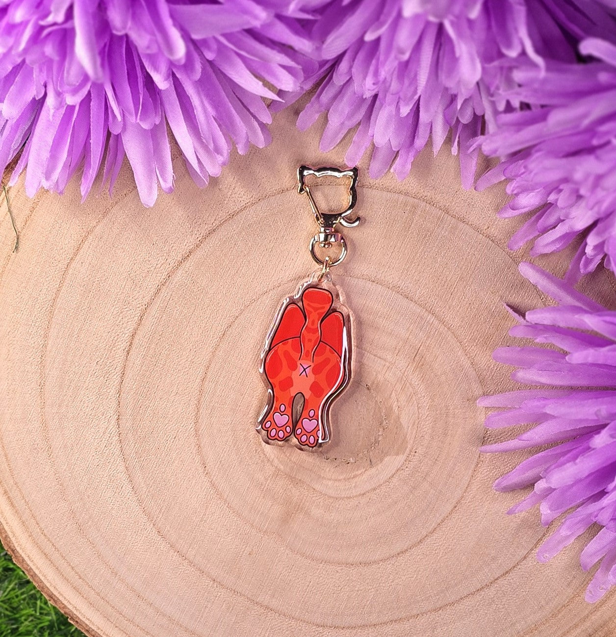 cat butt keyring on a wooden surface surrounded by purple flowers