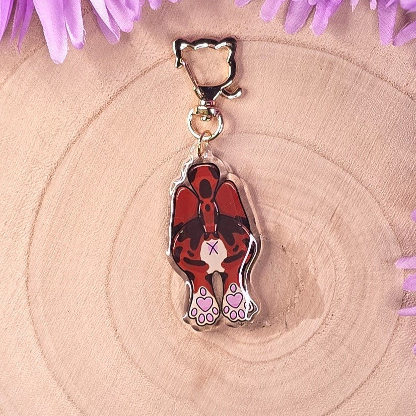 cat butt keyring design on a wooden surface with purple flowers.