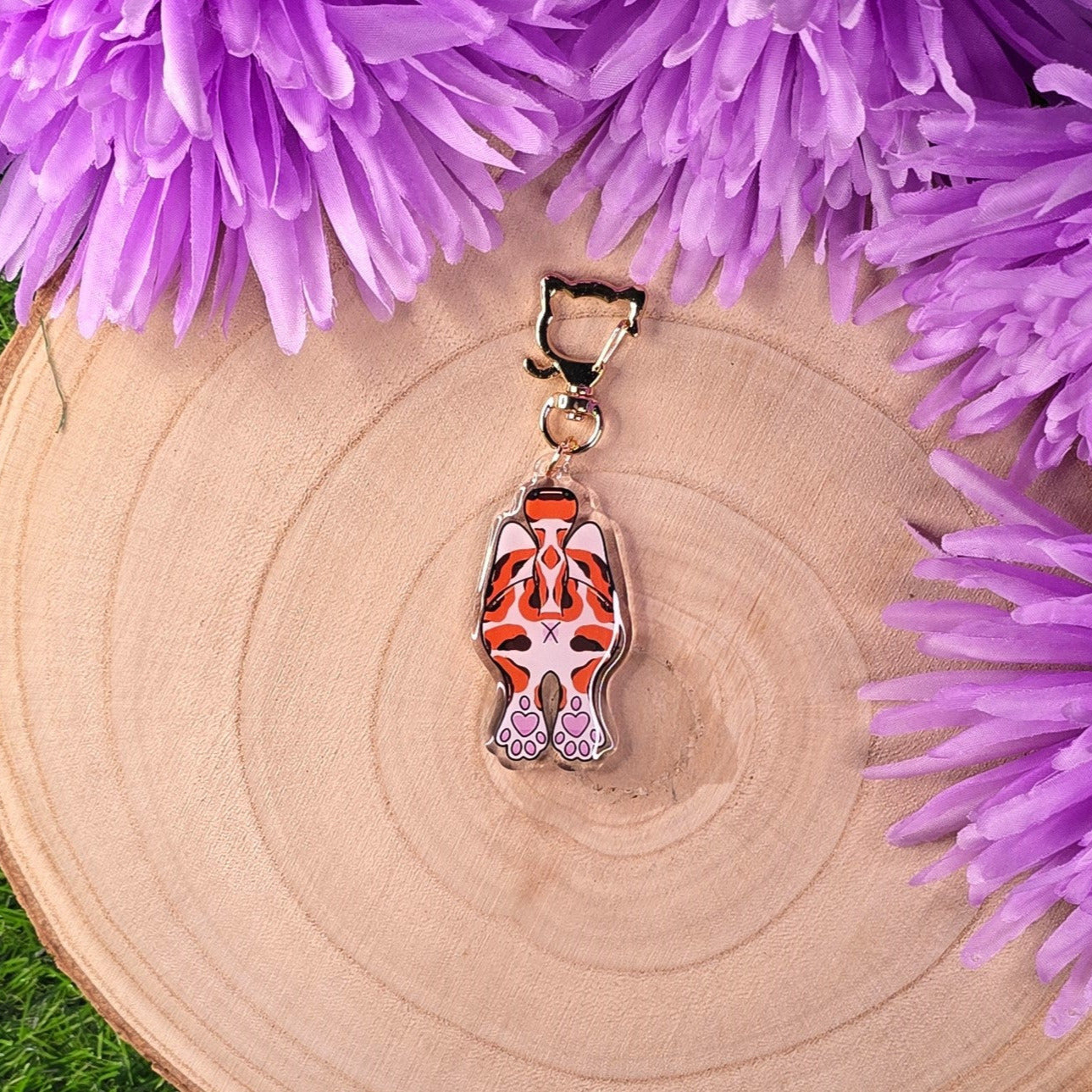 cat butt keychain on a wooden surface with purple flowers