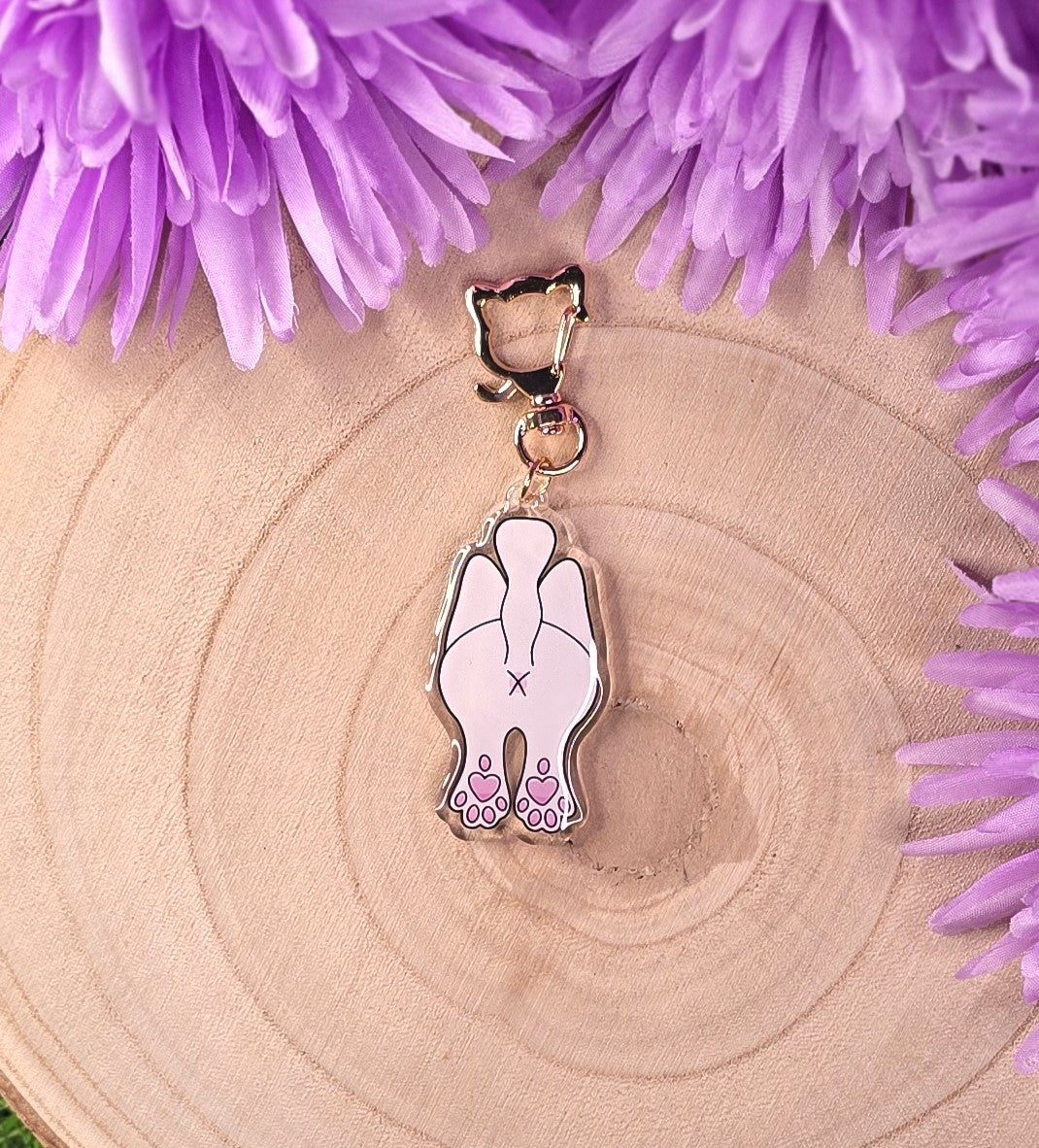 Cat-shaped keychain with paw design on a wooden surface with purple flowers